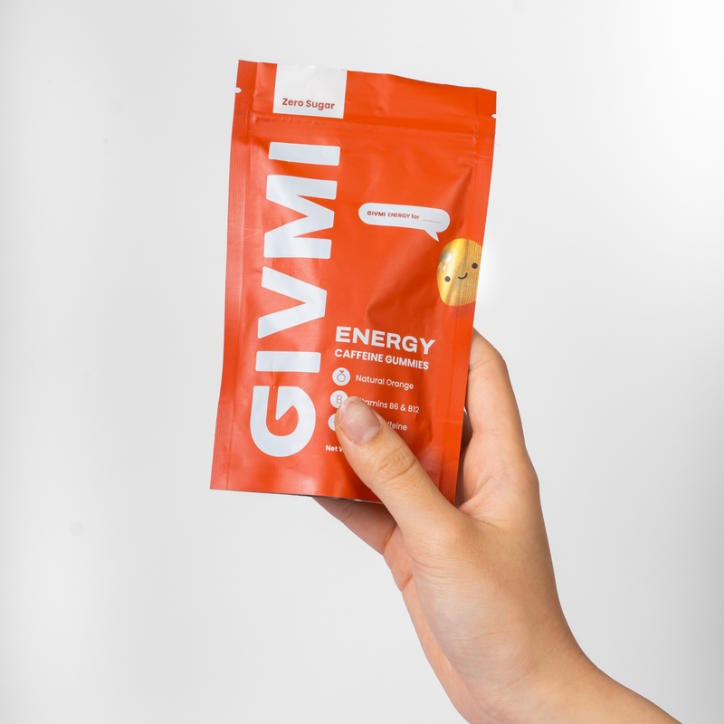 Hand holding a pouch of GIVMI ENERGY sugar-free caffeine gummies in vibrant orange packaging, enriched with Vitamins B6 & B12, for a natural energy boost.