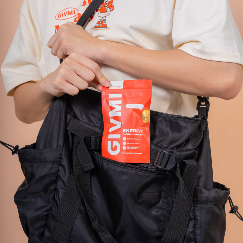 Person placing a pouch of GIVMI ENERGY sugar-free caffeine gummies into a black bag, highlighting portability and convenience for busy lifestyles.